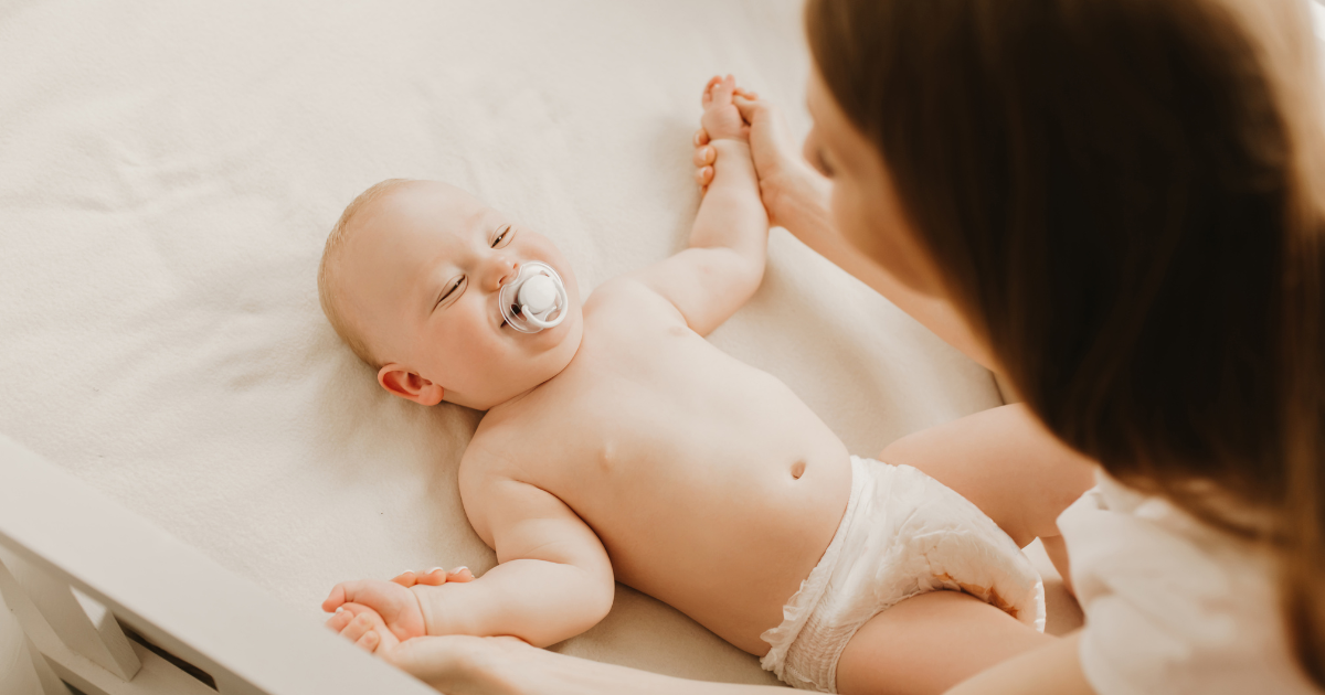 Bebé recostado sonriendo mientras su madre le toma las manitos