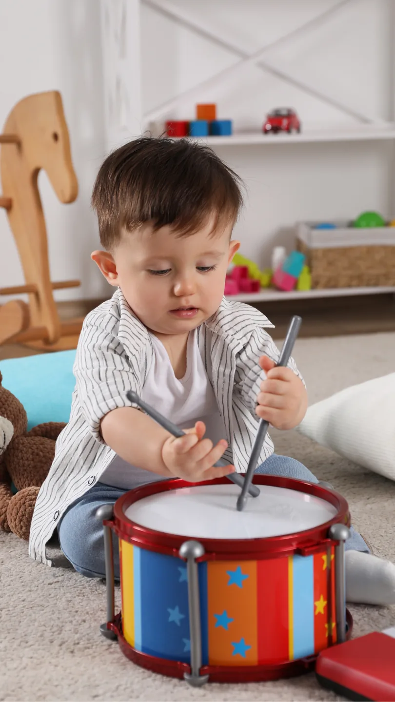 Niño pequeño sentado en el suelo tocando un tambor de juguete con baquetas