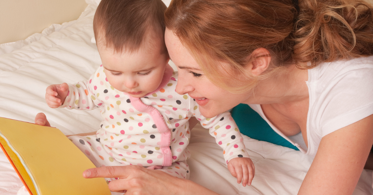 Una madre y su bebé leyendo juntos un libro de tapa dura sobre la cama